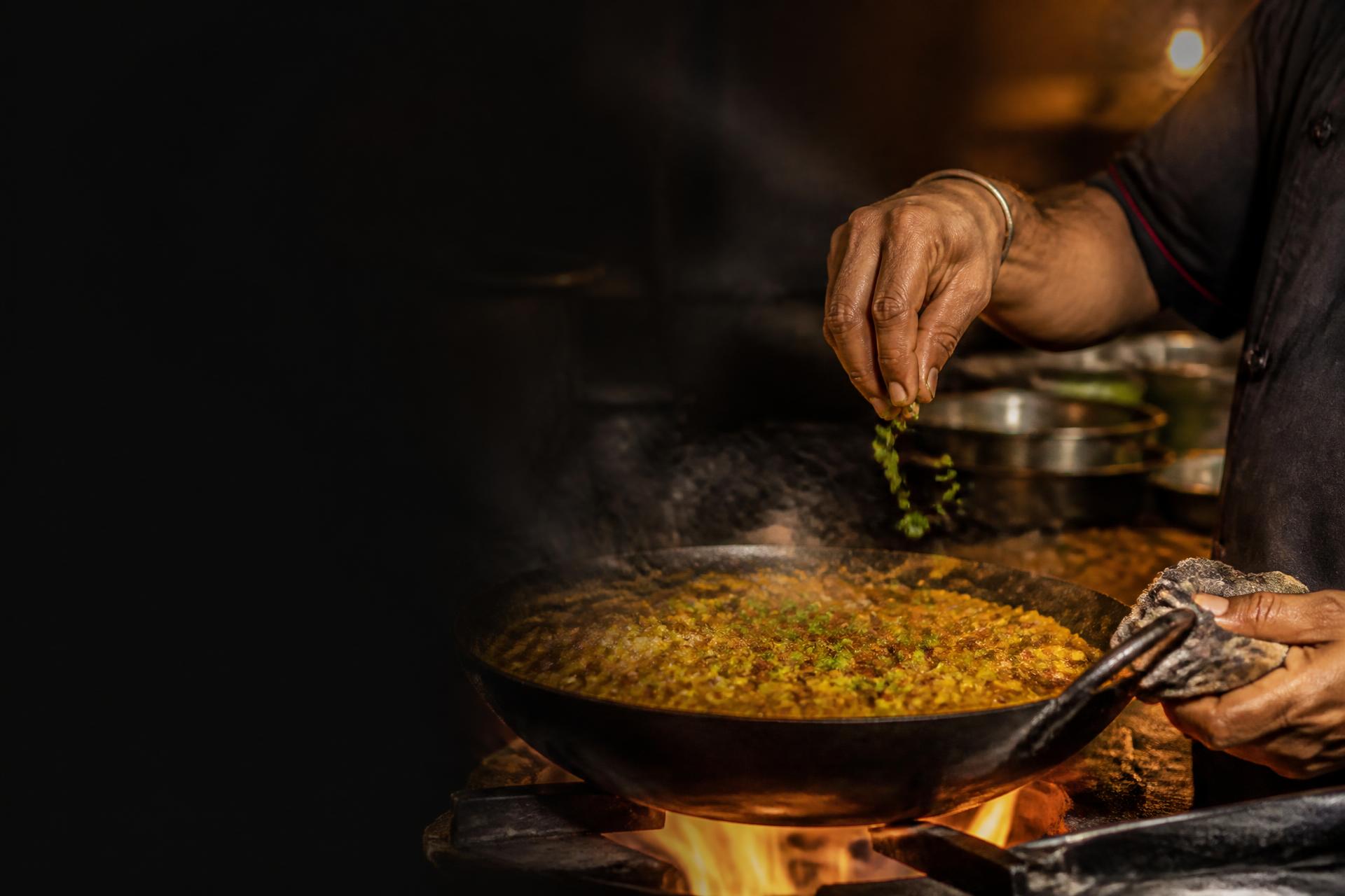 Koch vollendet eine Pfanne indisches Street Food über offener Flamme